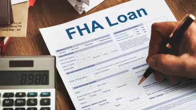 Close-up of hand filing out FHA Loan application on desk with calculator next to paper.