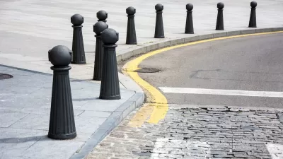 Black bollards lining a curved sidewalk next to a cobblestone street.