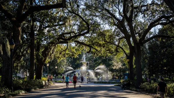 Paved path with artesian fountain at end and tall trees arching over walkway with joggers and walkers in Savannah, Georgia.