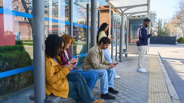 Young people at a bus stop all looking at their smartphones.