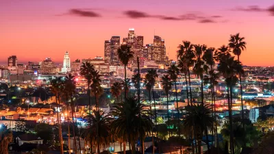 Nighttime view of downtown Los Angeles skyline with tall palm trees in foreground.