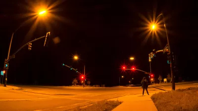 Intersection with stoplights at night with one pedestrian waiting to cross.