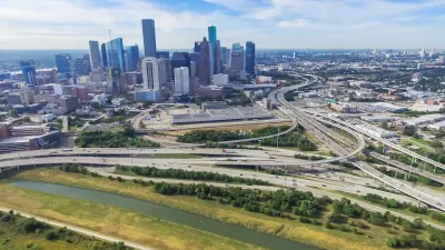 Aerial view of massive freeway interchange with downtown Houston skyline in background.