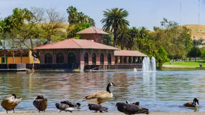 Canada geese and ducks on the shore of a lake with red brick boathouse in background across the lake in Lincoln Park, Los Angeles.