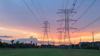 Electricity towers against sunset sky with green trees in background.