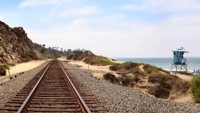 View looking down train tracks at San Clemente, California with grassy beach dunes and blue lifeguard tower on right side.