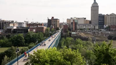A long pedestrian bridge over a river in the High Falls District with skyline of Rochester, New York, in the backround.