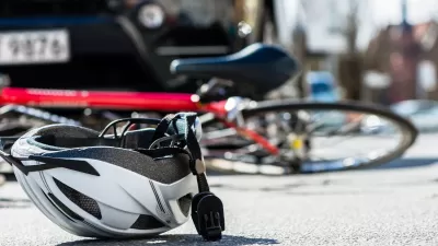 White bike helmet lies upturned on a road with red bicylce underneath the front of a far in the background.