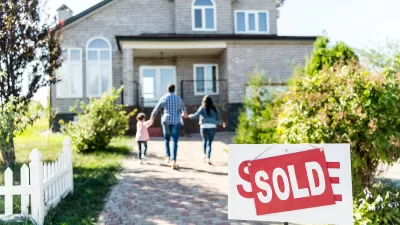 'For sale' sign with 'Sold' update in front of large single-family home with family of three walking toward house.