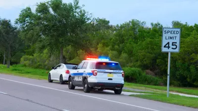 White and blue police SUV pulling over small white sedan in front of 45 mph speed limit sign.