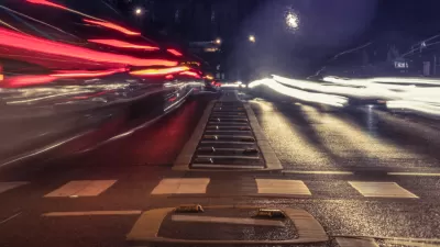 Low view of empty crosswalk at night from middle of street with blurred cars speeding by on both sides.