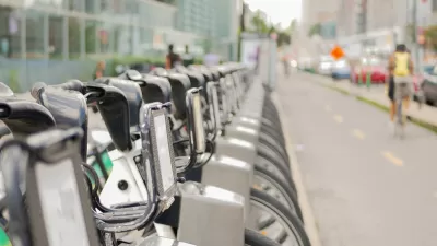 Close-up of silver Bixi bike share bikes parked at a station in Montreal, Quebec, Canada with blurred person on bike riding away in background.