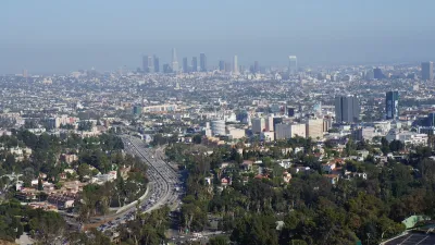 Downtown Los Angeles skyline viewed from a distance with freeway and trees in foreground.