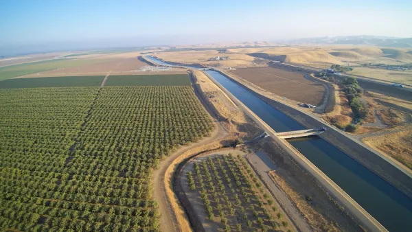 Aerial view of Claifornia aqueduct with green orchard on one side.