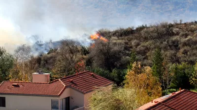 Wildfire approaching stucco house with red tile roof.