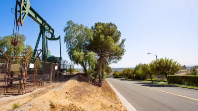Green oil well behind a fence next to a small street in California.