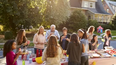 Group of people standing around a table with food in front of homes during a block party.