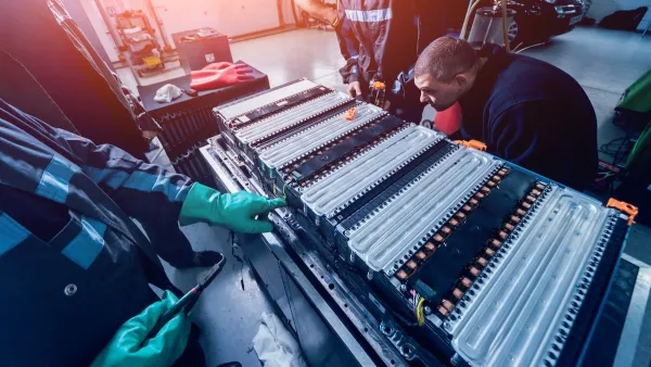 Two workers disassembling a set of leectric car batteries in a factory.
