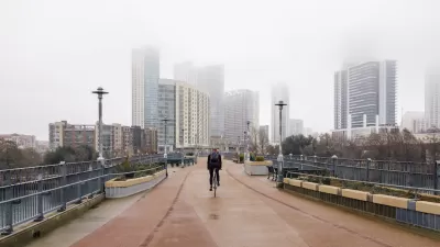 One cyclist rides on pedestrian bridge with foggy Austin, Texas skyline in background.