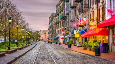 Cobblestone street with streetcar line, row of vintage streetlights on left, and colorful restaurant and shop awnings on right on River Street in Savannah, Georgia.