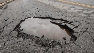 CLose-up of pothole in asphalt road filled with water reflecting grey cloudy sky.
