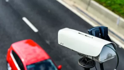 Close-up of speed camera mounted above roadway with red car passing by underneath