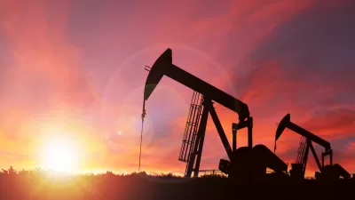 Oil well pumpjack sillhouetted against a bright pink sunset sky.