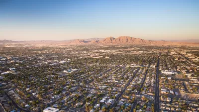 Aerial view of sprawling Las Vegas suburbs at golden hour with desert mountain in background.