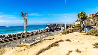 Silver and blue train passing by on track at the edge of Pacific Ocean in San Clemente, California.