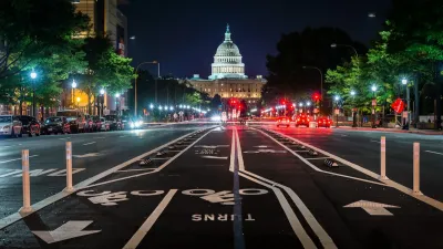 Low view of separated bike lanes in middle of Pennsylvania Avenue with U.S. Capitol dome visible at end of street at night.