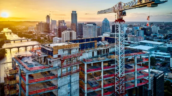Large tower under construction with crane with American and Texas flags in downtown Austin, Texas against sunset sky.