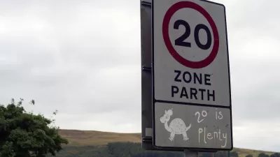 Close-up of white 20 kph speed limit sign in Europe with cartoon turtle and '20 is plenty' sticker underneath.