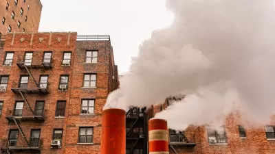 Orange and white steam pipes in New York City releasing white steam against background of red brick buildings.