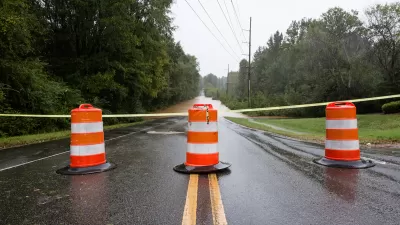 Orange and white barrels with yellow caution tape blocking flooded road.