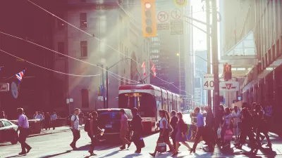 Pedestrians in busy crosswalk with tram in background in downtown Toronto, Canada with sunrise or sunset light in background.