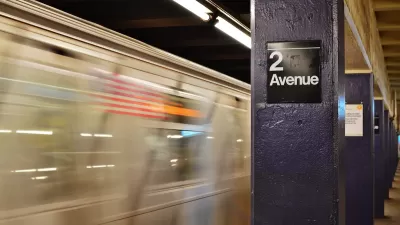 View of 2nd Avenue sign on concrete column on subway platform with blurred train speeding past in New York City.