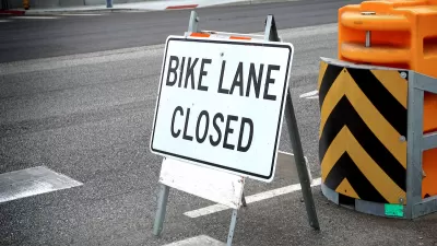 "Bike Lane Closed" A-frame sign on street with yellow and black barricade behind it.