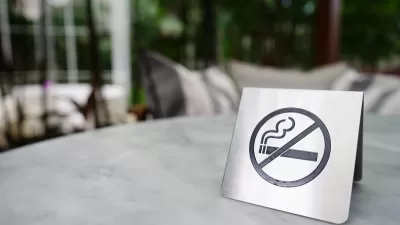 Close-up of silver sign indicating 'no smoking' with cigarette inside circle with line. Sign is sitting on patio table outdoors.