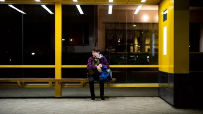 Yellow bus shelter with one young person sitting on bench at night.