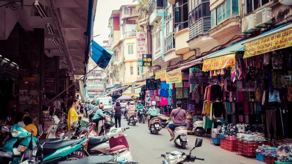 People on motorbikes driving through busy vibrant Hanoi, Vietnam produce market.