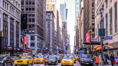 Intersection on Manhattan street with yellow cabs and black cars waiting for stoplight.
