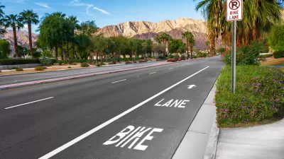 Marked bike lane on wide asphalt street with palm trees and Los Angeles mountains in background.