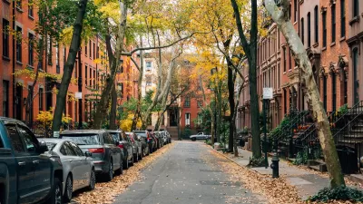Small New York City street with brownstone homes and cars parked on one side.