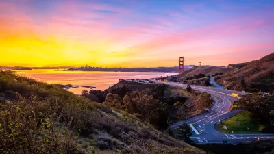 View of windy road in Marin County and Golden Gate Bridge and San Francisco skyline in background at sunrise.