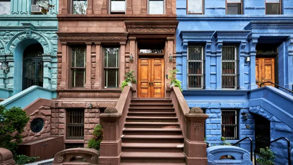 Colorful teal, brown, and blue brownstones in New York City with wide stone stairways going up to first floor doors.