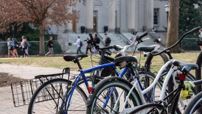 Close-up of crowded bike rack on university campus with students walking in background.