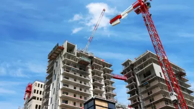 View of top of high-rise apartment building under construction with red and white cranes