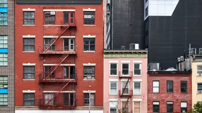 Three brick apartment buildings of various heights with fire escapes in New York City.