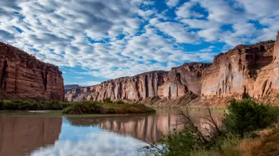 View of Colorado River winding through canyon in red rock cliffs against lightly cloudy blue sky