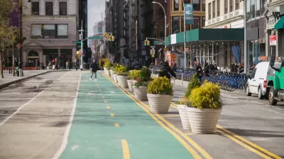 Green painted bike lane in New York City protected by concrete planters with Citi Bike station visible in background on sidewalk.